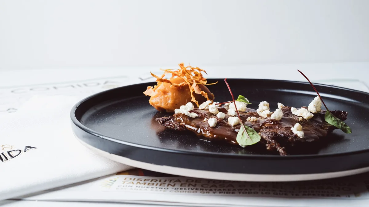 Plato de carne con crujiente sobre mantel en el restaurante Vida & Comida de Salamanca